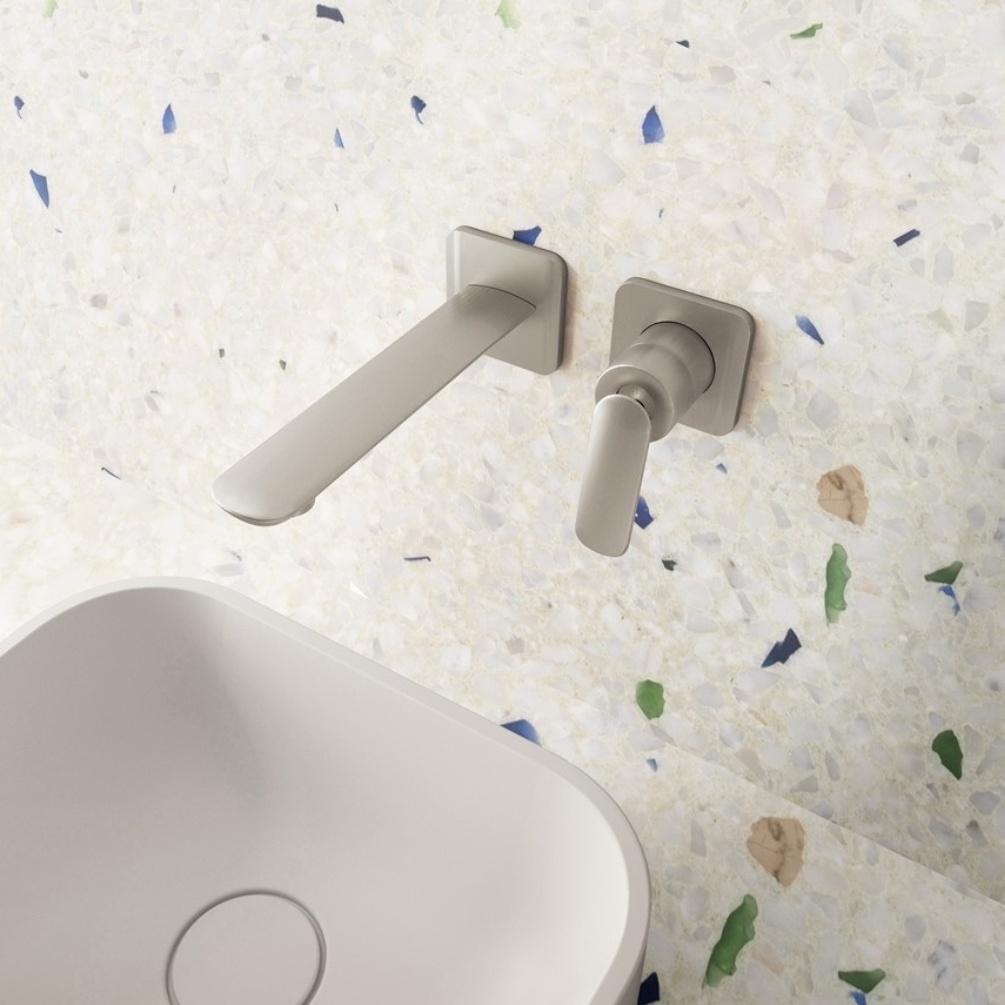 Lifestyle image of the Crosswater Huck Brushed Stainless Steel Wall Mounted Basin Mixer installed on a terrazzo wall, above a white countertop basin